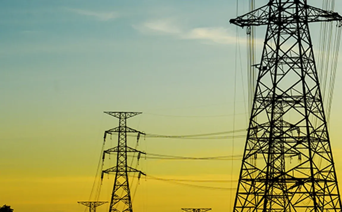 Torres de transmisión eléctrica con cables de alta tensión en un paisaje de atardecer.